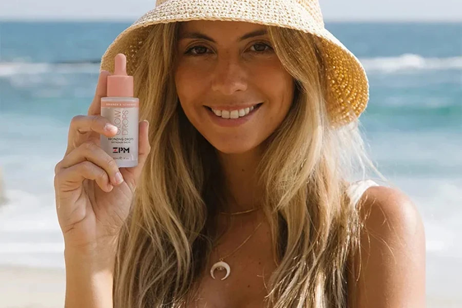 Femme tenant des gouttes bronzantes sur la plage