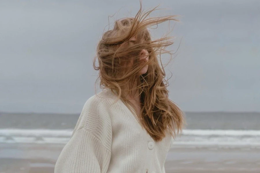 Woman wearing a neutral colored, knit cardigan on the beach