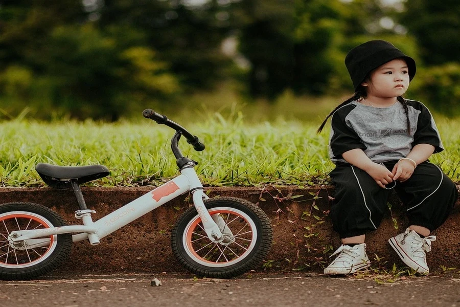 Seorang anak laki-laki duduk dengan sepeda yang diparkir di dekatnya