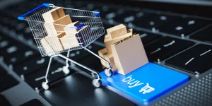 a shopping cart filled with items stands on a laptop keyboard with a buy button
