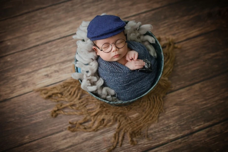 A sleeping baby wearing a hat and glasses wrapped in a swaddle
