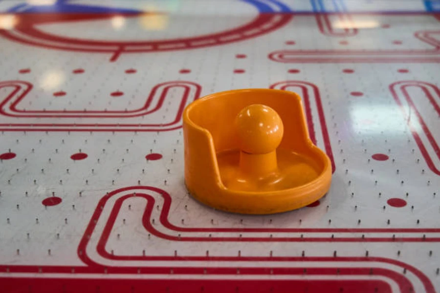 Air hockey table with orange paddle sitting on playing surface