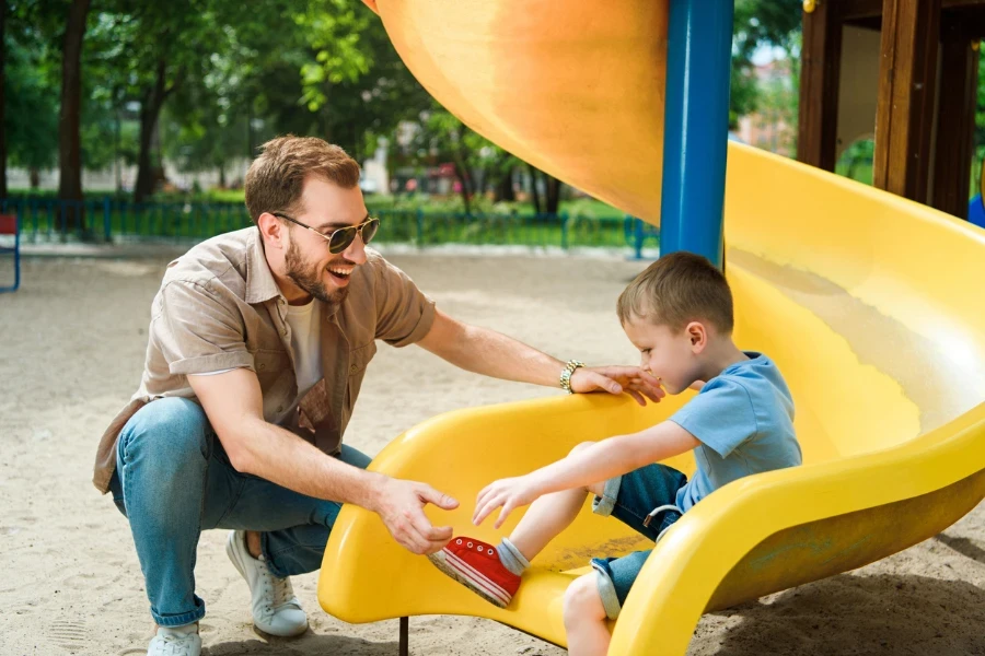 Boy playing on yellow playground slide with his father