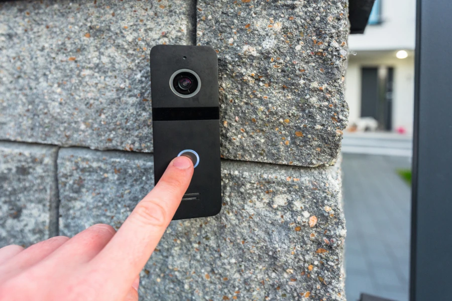 Hand pressing a video doorbell mounted on a stone wall