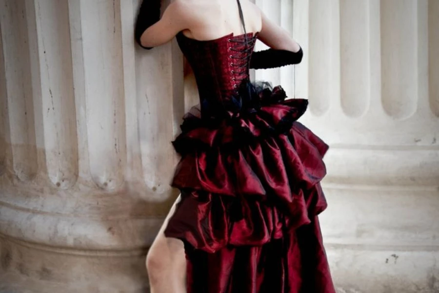 Lady posing near a pillar in a red lace dress with corset top