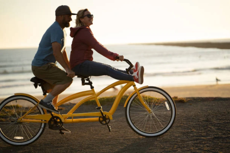 Man and woman riding yellow tandem bike on beach