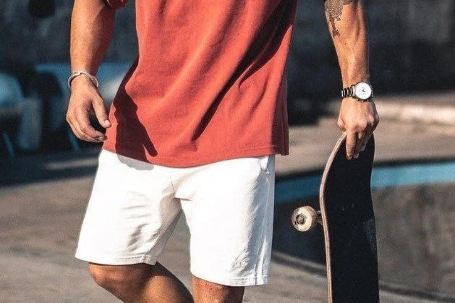 Man holding a skateboard wearing white shorts