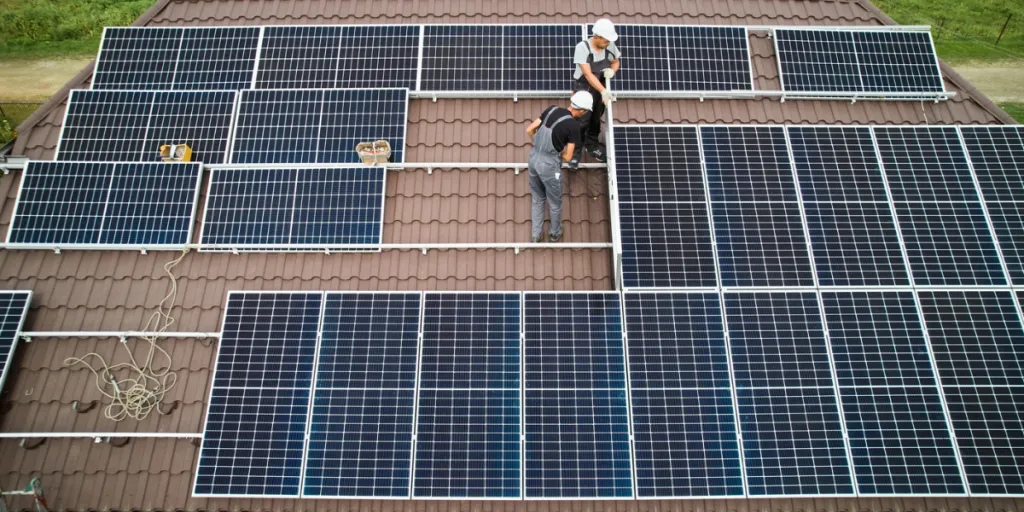 men technicians mounting photovoltaic solar moduls on roof of house