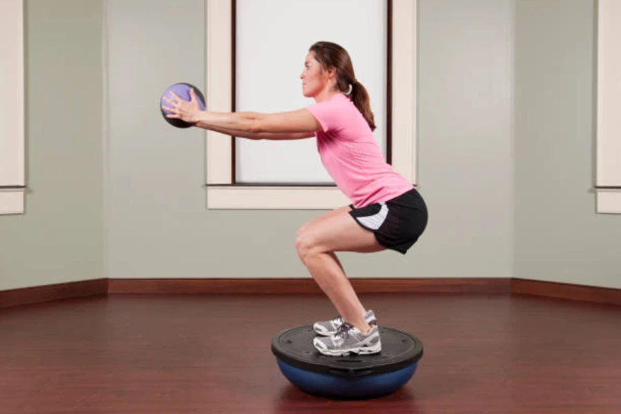 Persona de pie sobre una pelota de equilibrio azul en posición de cuclillas