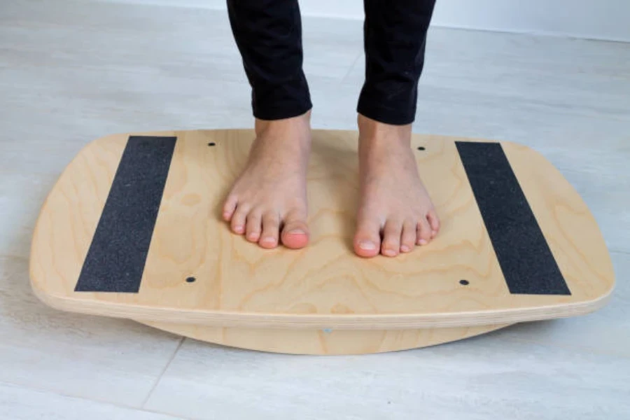 Persona de pie sobre una tabla de equilibrio de madera con los pies descalzos