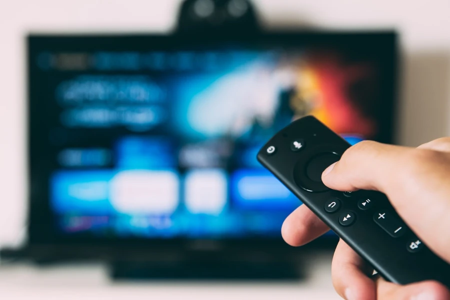 smart tv blurred behind a hand holding a smart remote