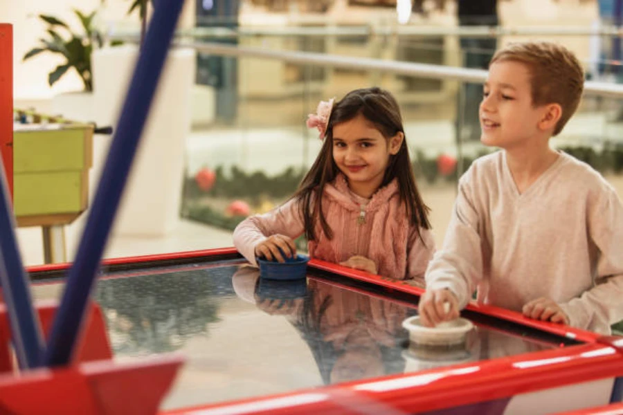 Two children playing air hockey inside shopping center