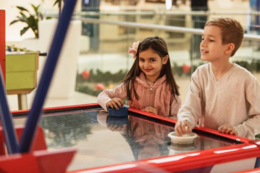 Dos niños jugando air hockey dentro del centro comercial