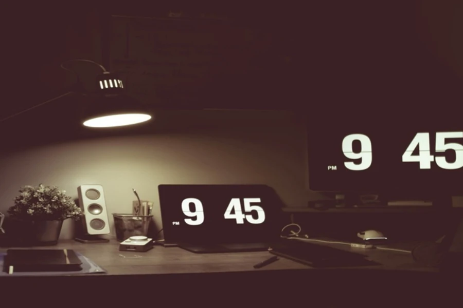 Two digital alarm clocks on a desk lit by a lamp