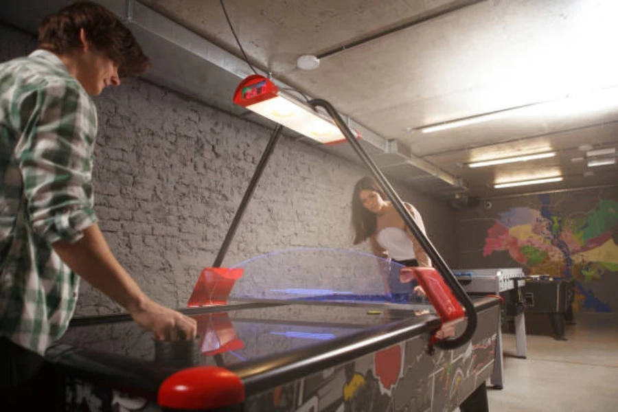 Dos personas jugando con una mesa de air hockey que funciona con monedas