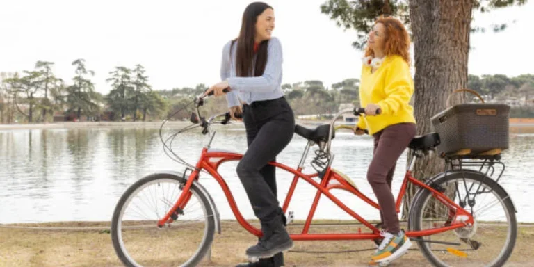 Two women riding red tandem bike along a lake