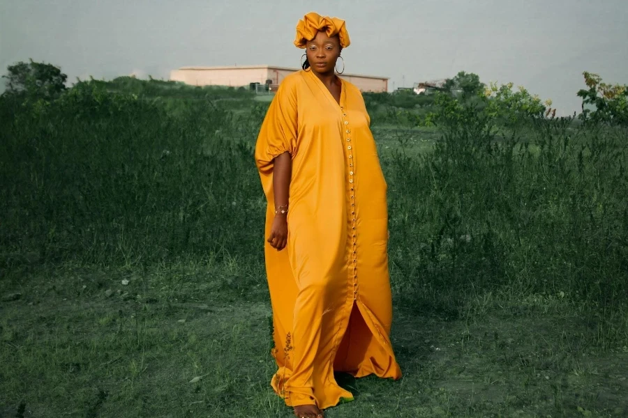 Frau in einem orangefarbenen langen, voluminösen Kleid und passendem Kopfschmuck