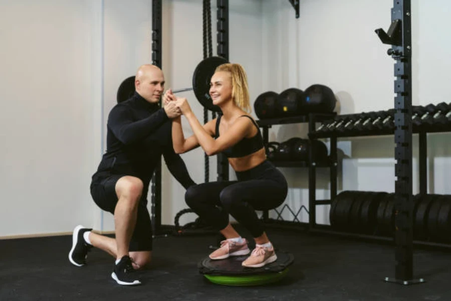 Woman squatting on a balance ball beside her coach