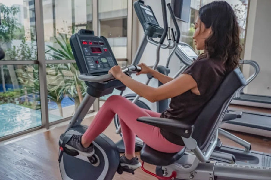 Mulher usando uma bicicleta reclinada em frente a uma grande janela