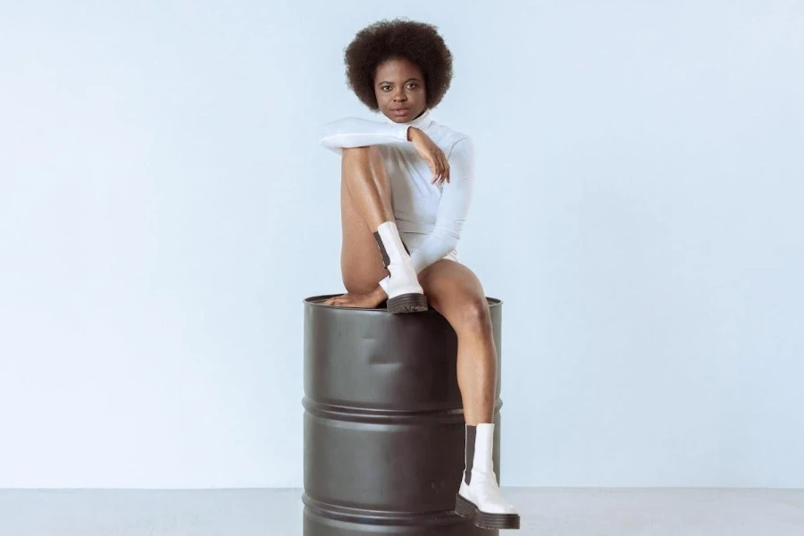 Woman wearing a white bodysuit and sitting on a barrel