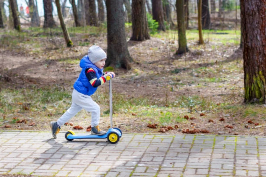 Young boy pushing a three wheel scooter in park