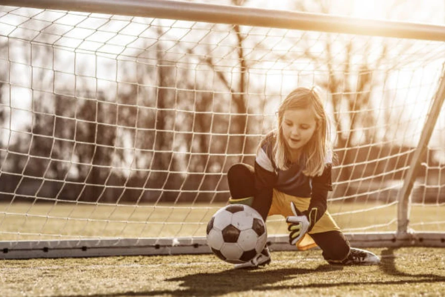 Niña en una pequeña red atrapando una pelota de fútbol rodante