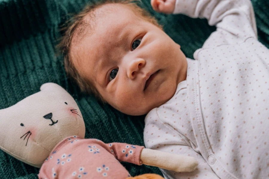 Un bébé allongé à côté d'une poupée en peluche