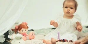 Seorang gadis berusia satu tahun dengan kue ulang tahun dan boneka