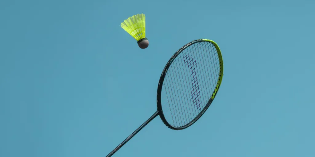 black and yellow badminton racket hitting yellow shuttlecock in air