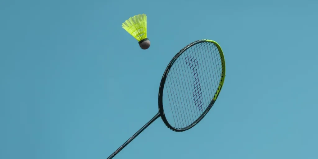 raqueta de bádminton negra y amarilla golpeando un volante amarillo en el aire