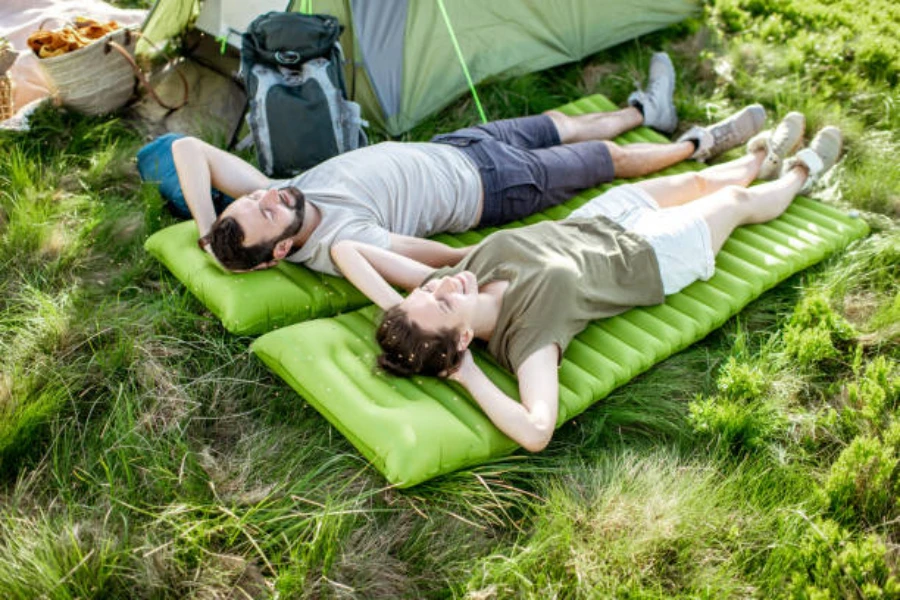 Couple relaxing on individual self inflating mattresses on grass