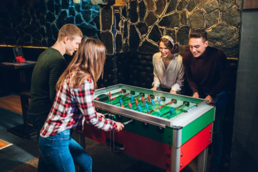 Quatro pessoas jogando em uma mesa de pebolim profissional dentro de casa