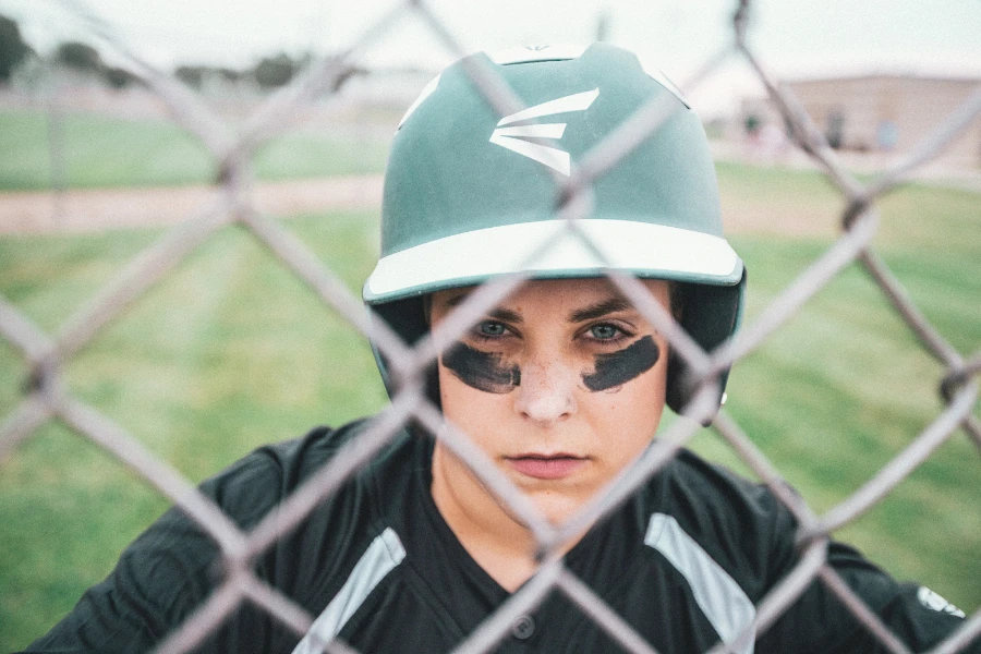 Senhora atrás de uma cerca de arame usando um capacete de beisebol