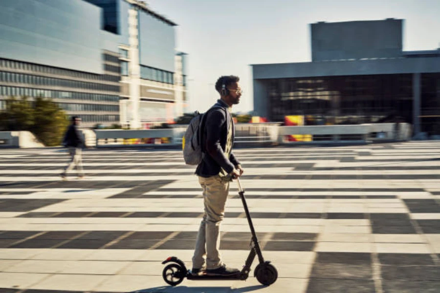 Man riding a black scooter through a large public square