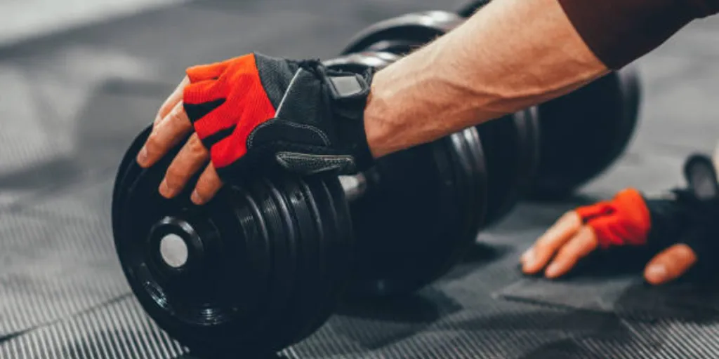 Man wearing red weightlifting gloves while touching dumbbell