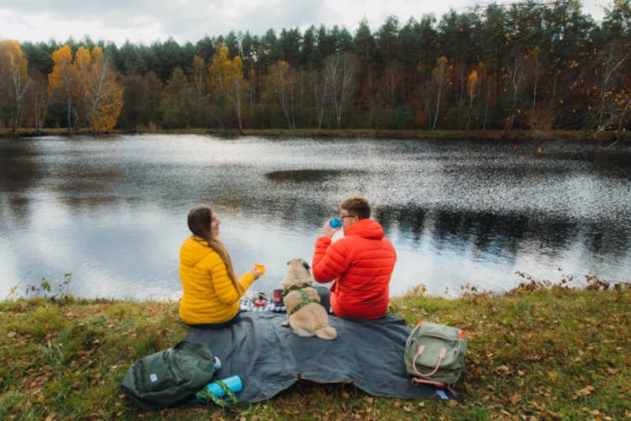 Man, woman, and dog sitting on blanket next to lake