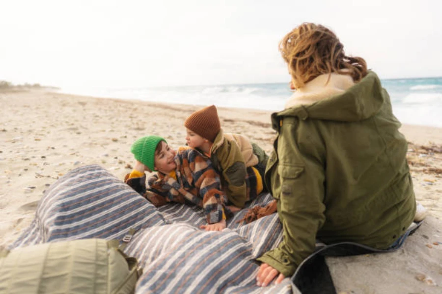 Mother and sons sitting on quilted picnic blanket at beach