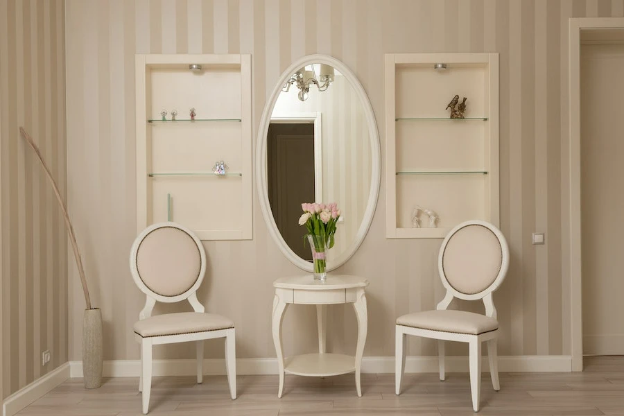 Oval wall mirror hung on a wall with two vanity chairs