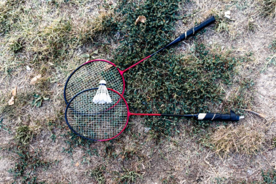 Pair of red and black badminton rackets laid on grass