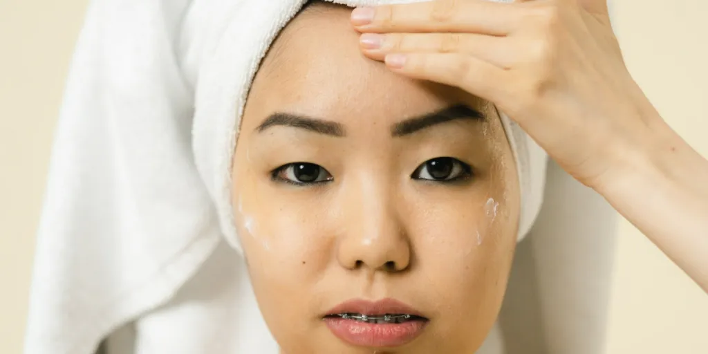 Person with a towel on their head applying face moisturizer