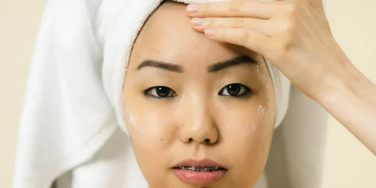 Person with a towel on their head applying face moisturizer