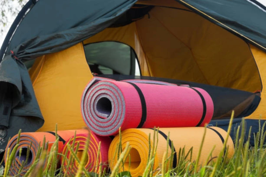 Stack of multi-colored camping mats folded next to tent