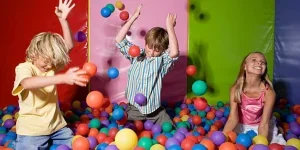 Three children playing in a colorful ball pit indoors