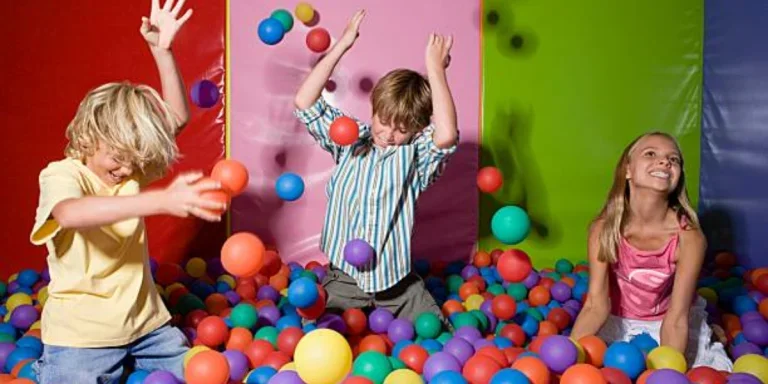 Three children playing in a colorful ball pit indoors