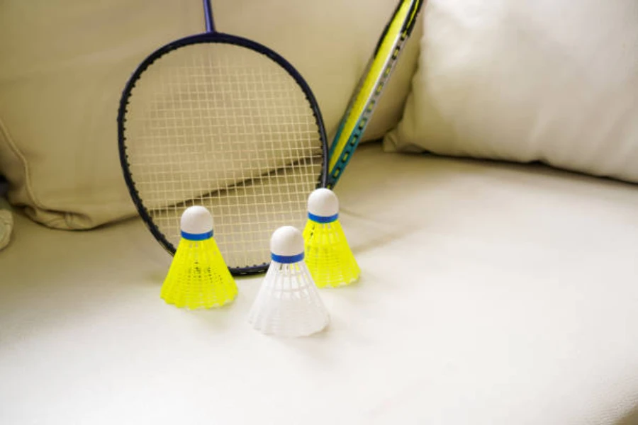 Three plastic shuttlecocks on couch next to badminton racquets