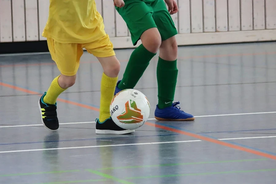 Two kids kick a ball during an indoor soccer match