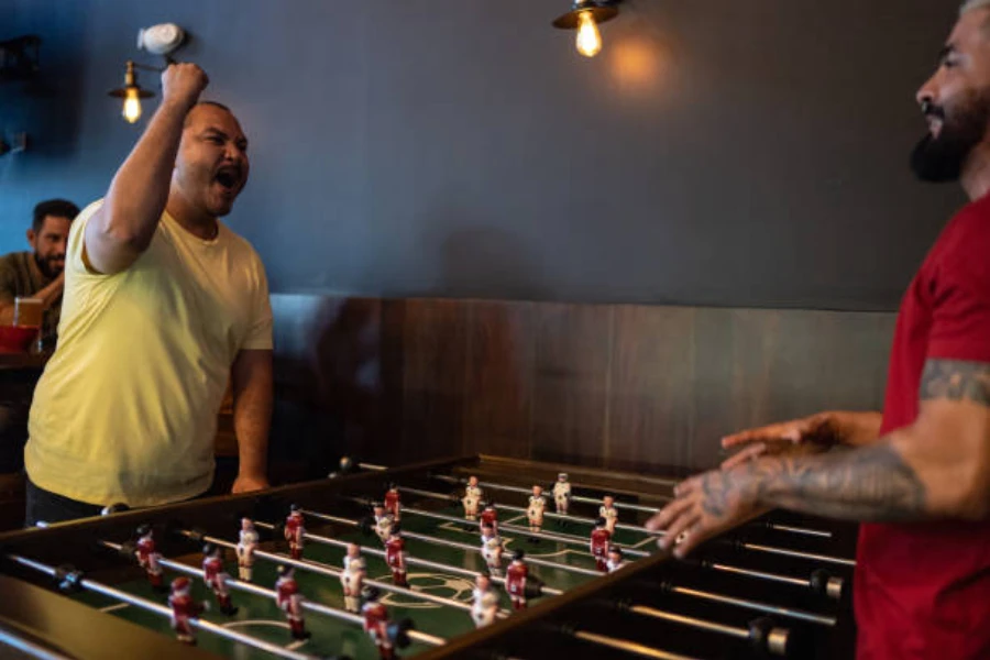 Two men playing foosball for fun inside a bar