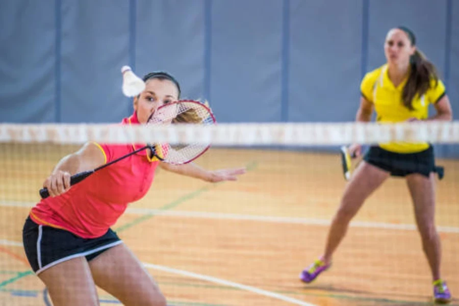 Two women playing doubles on an indoor badminton court