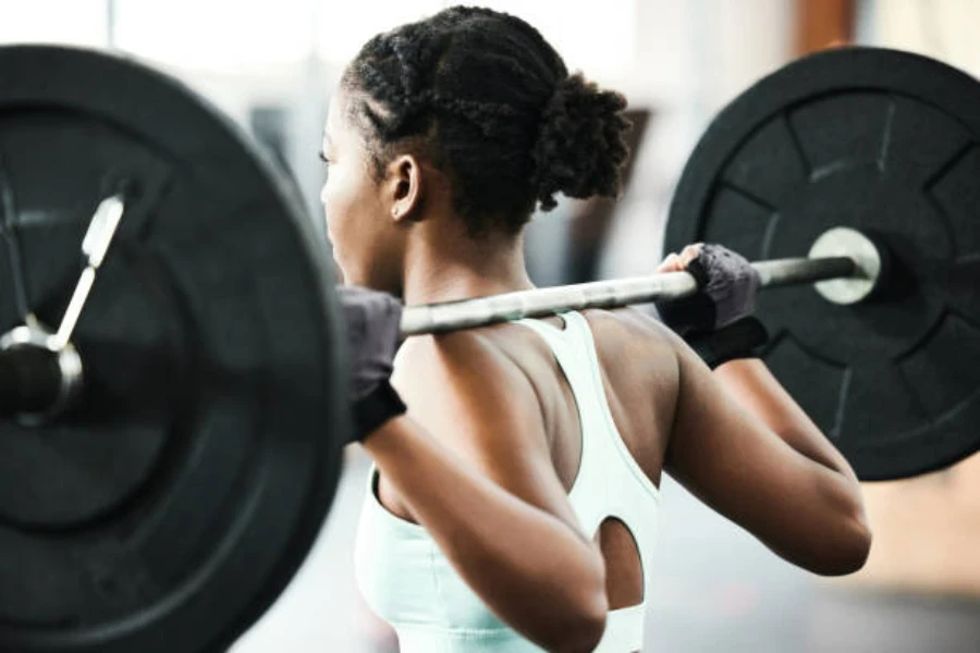 Woman holding barbell on her back while wearing weightlifting gloves