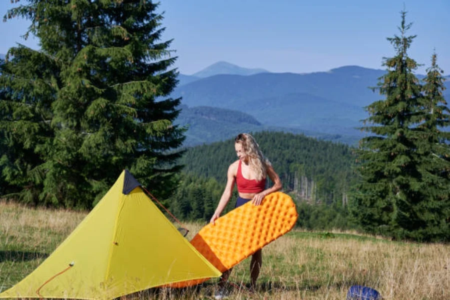 Femme tirant un tapis de camping orange hors de la tente